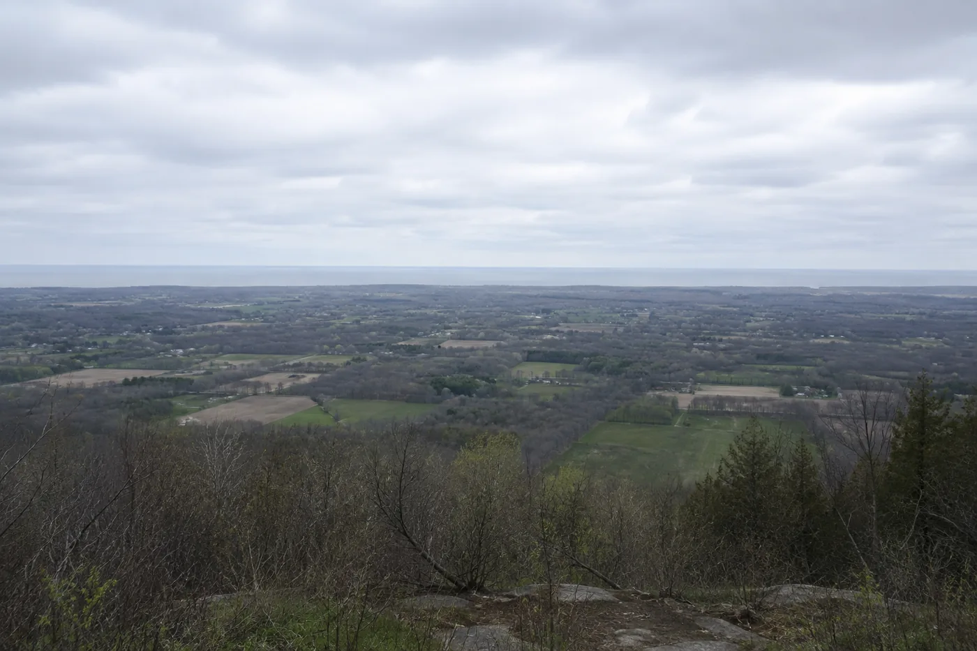 Farmland and small town rooftops seen from the Niagara Escarpment, with Lake Ontario in the distance.